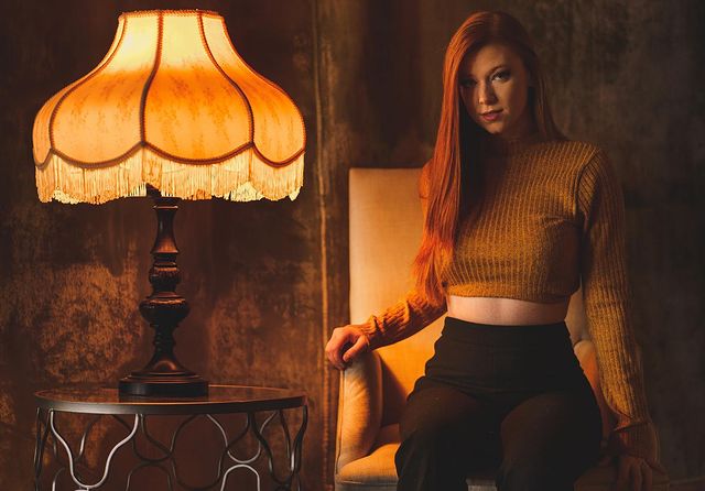 Megan DeLuca sitting beside a lamp in orange light while wearing a yellow crop top